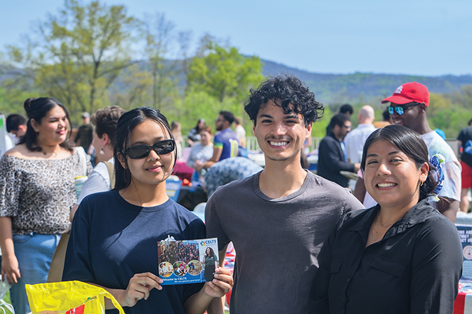 Three students smile at the camera and hold up a card