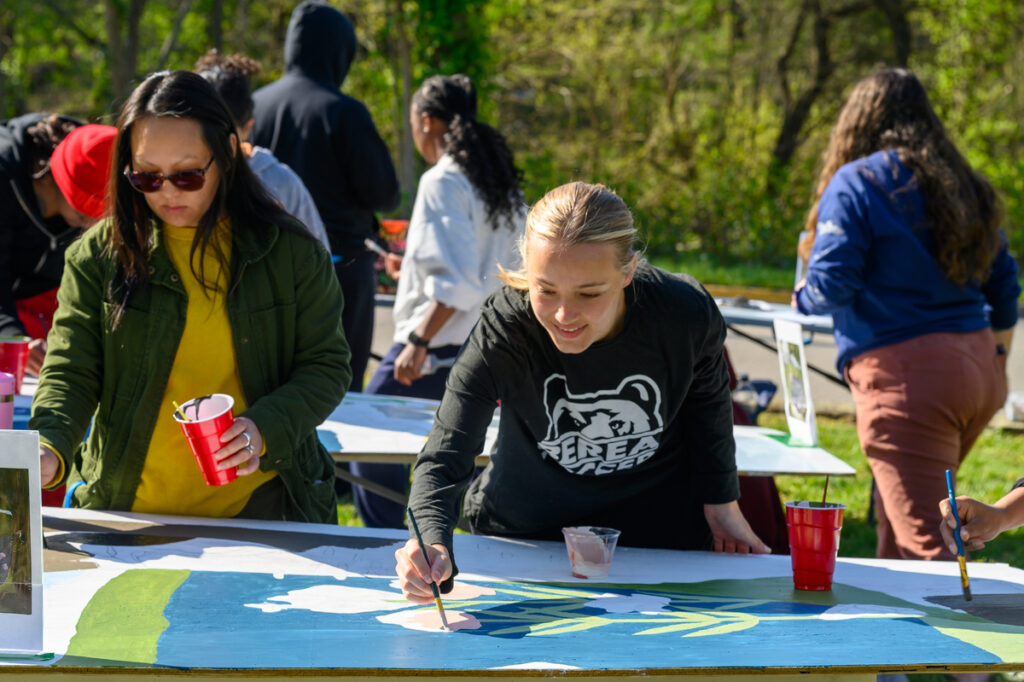 Student in a Berea Women's Soccer shirt painting a large mural