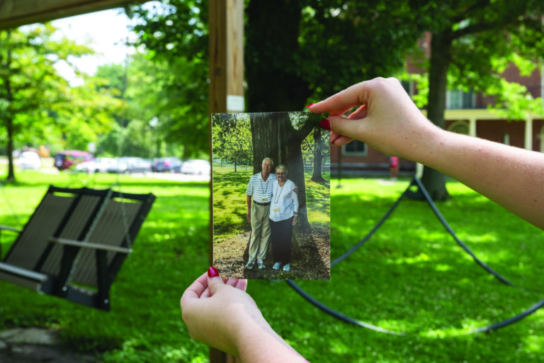 Hands hold a family photo of Martha Salter '51 and Ohlen Wilson '50 in front of the tree where they would meet up for dates on Berea College's Campus. The tree can be seen in the background of the original photo as well.